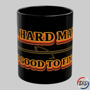 A black ceramic coffee mug featuring bold retro orange‑and‑yellow gradient typography that reads “A Hard Man Is Good to Find,” with a vintage horizontal accent line and small star details.